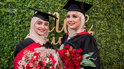 A pair of graduates posing while holding a bouquet of flowers