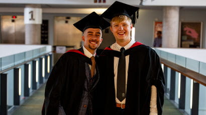 A pair of graduates posing while holding a bouquet of flowers