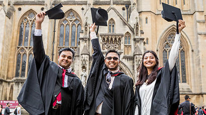 Three graduates raising their caps outside Bristol Cathedral