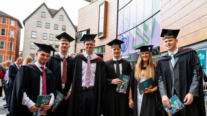 Three graduates raising their caps outside Bristol Cathedral