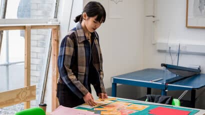 Art student arranging printed designs on a table.