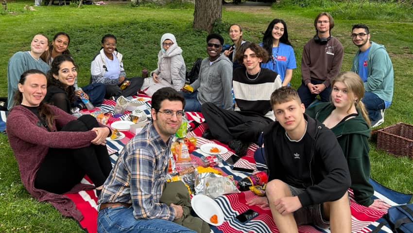 A large group of students enjoying a picnic in a green space on campus.