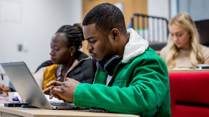 Students sitting in a hall listening to a lecture and taking notes.