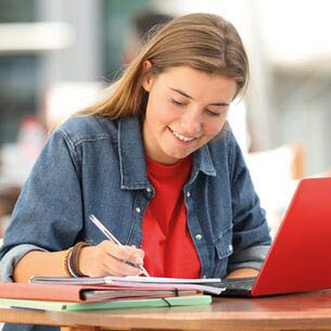 Student taking notes next to her laptop