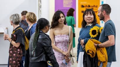 A group of people standing and talking in a gallery space with colourful artwork on the walls.