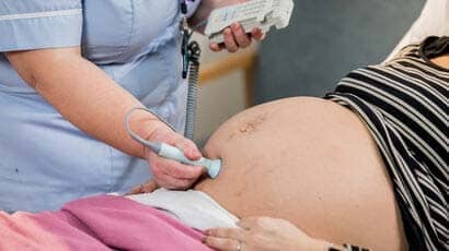 Student nurse using medical equipment on a pregnant women stomach