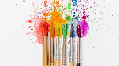 6 paint brushes resting on a canvas covered in splattered paint