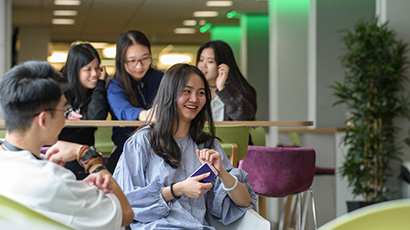 Group of five students sat talking together on colourful chairs.