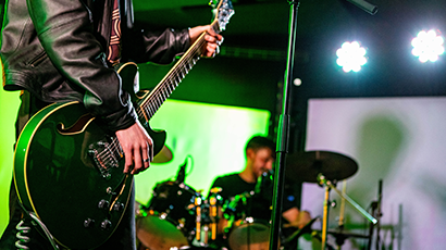 Image of guitar being played with drummer in background