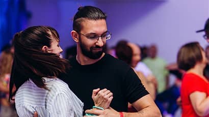 Close up of a a man and woman dancing salsa with many other couples dancing in the background.