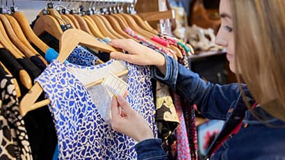 Woman examining the price tab label on a top in front of a rack of clothes. 