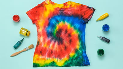 A rainbow spiral tie-dye t-shirt with pots of dye and brushes around it.