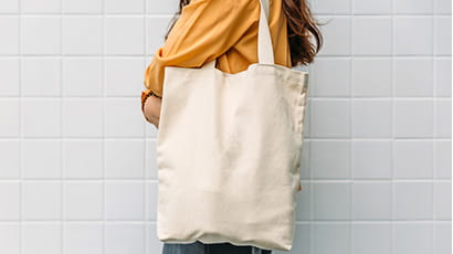 Person in a mustard-colour shirt standing with a plain tote bag hanging from shoulder. 