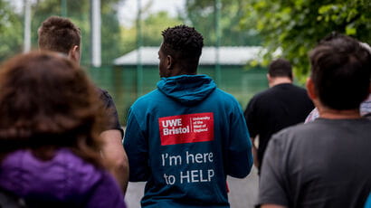 UWE Bristol tour guide leading a group of people around campus wearing a jumper that says 'I'm here to help' on the back.