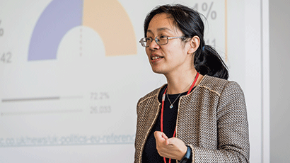 Woman presenting to class with a projector showing a graph on the wall behind her.