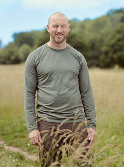 Postgraduate student James, standing in a field, surrounded by grass