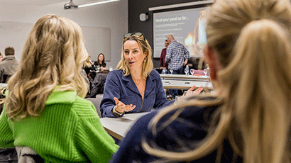 Business woman talking to two students with their backs to camera at a seminar room table.