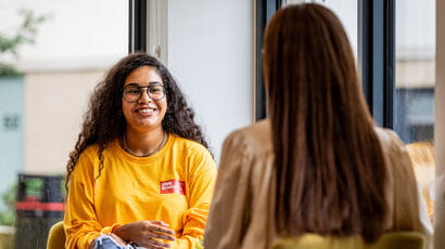 Student Life rep wearing a yellow branded jumper talking to a student.