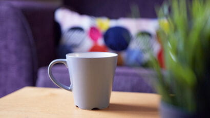 Cup of tea and a plant on a coffee table with a comfy sofa in the background.