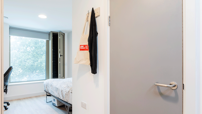 Looking into a bedroom at Kingfisher Court with bed, clothes hooks and desk space.
