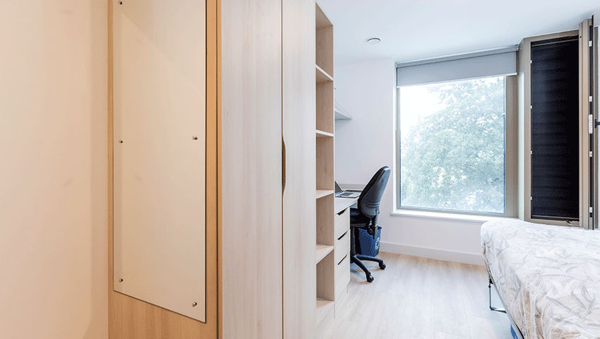 Looking into a bedroom at Kingfisher Court with a bed, wardrobe, full-length mirror and desk.