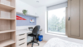 A bedroom desk space with chair and high shelf.