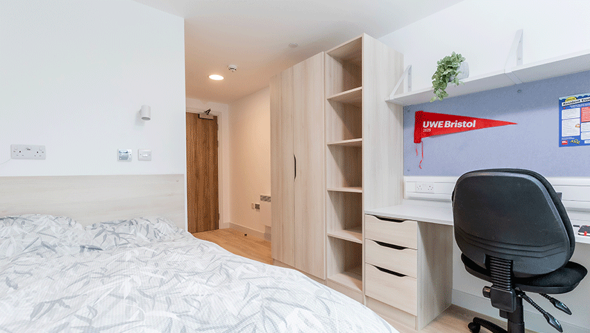 A standard bedroom at Kingfisher Court with a bed, wardrobe and storage and desk with chair.