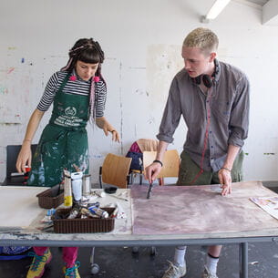 Two art students working on a project at a drawing table.