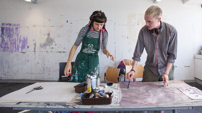 Two art students working on a project at a drawing table.