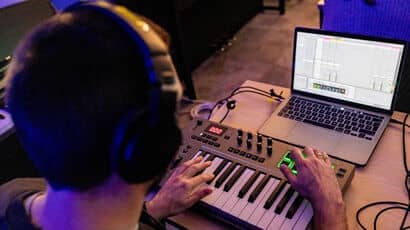 A white man with a laptop and electronic piano keyboard mixing sound.