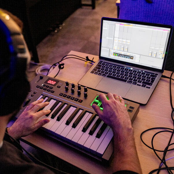 A white man uses a electronic music keyboard and computer to do some music production.