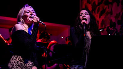 Two women singing into microphones on a stage