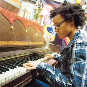 Woman in check shirt playing an upright piano.