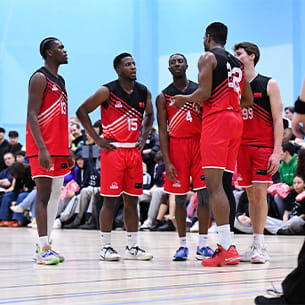 Group of performance sport athletes dressed in red uniform having a team huddle on the basketball court.