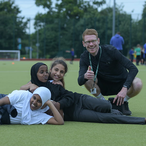 UWE Sports Volunteer with a group of school pupils on a football field, smiling with their thumbs up.