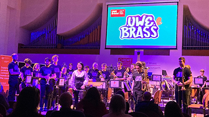 brass band standing on stage with large UWE Brass blue logo on the screen