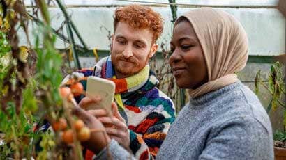 A couple of people looking at a crop and taking a photo of it.