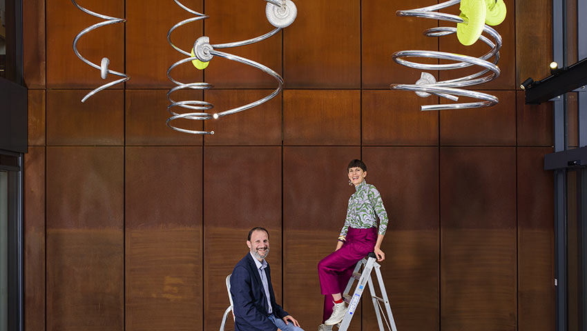 Alice Channer and Professor Ioannis Ieropoulos on a ladder with her 'Nanowires' sculpture in the Engineering Building. Photo credit: Thierry Bal, 2021.