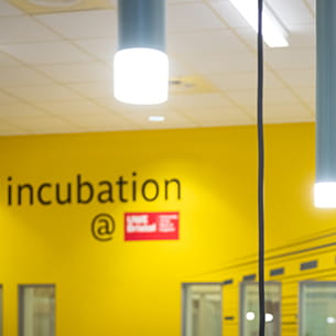 Top view of Launch Space showing the hanging lights and the word 'Incubation' with the UWE Bristol logo on the yellow wall.