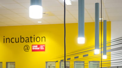 Top view of Launch Space showing the hanging lights and the word 'Incubation' with the UWE Bristol logo on the yellow wall.
