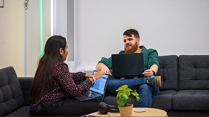 A white male and Asian female sitting on sofas facing each other and having a discussion in Launch Space.