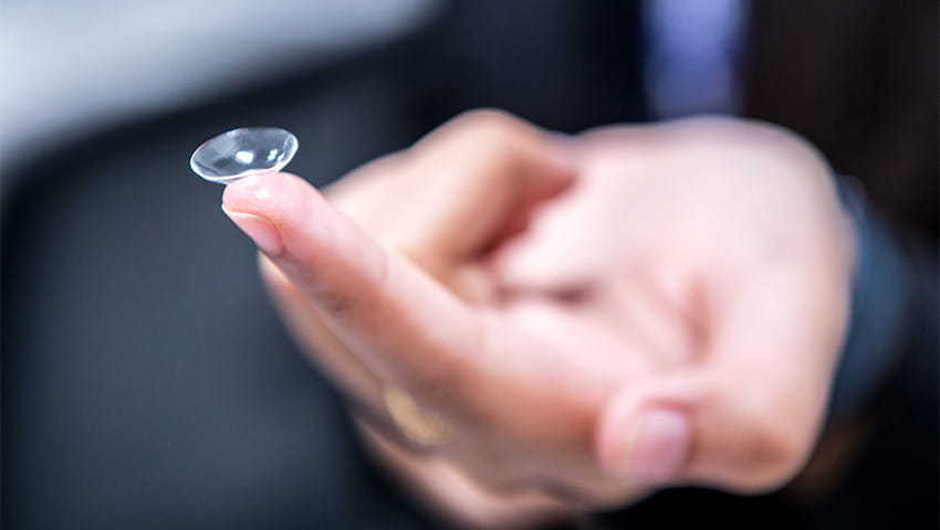 A close-up of someone holding a contact lens on their finger.