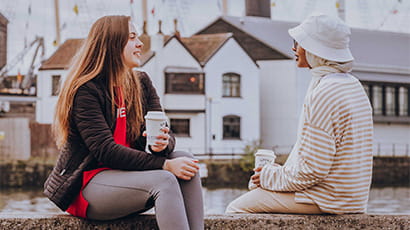 Two students sitting by the harbour drinking coffee