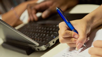 Close up of hands writing on a computer.