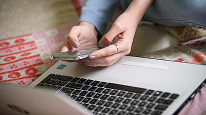 Hands holding a mobile phone next to a laptop