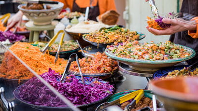 Person serving colourful falafel and salad at a food market.