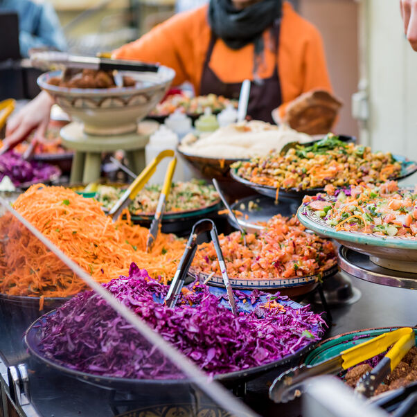 Person serving colourful salad with falafel at a food market.