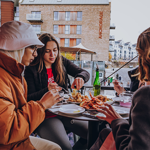 A group of students sat around a cafe table outdoors eating a selection of dishes.