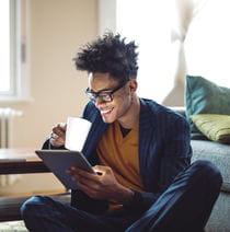 Person reading on an iPad while drinking from a mug.