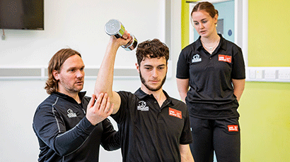Patient being aided while using dumbbells in a shoulder exercise.